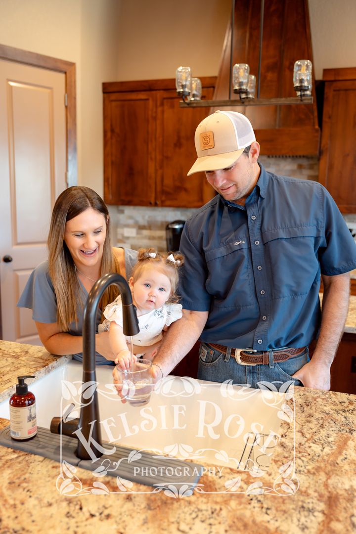Young family with baby filling up a glass of water at their kitchen sink in modern home with granite countertops.