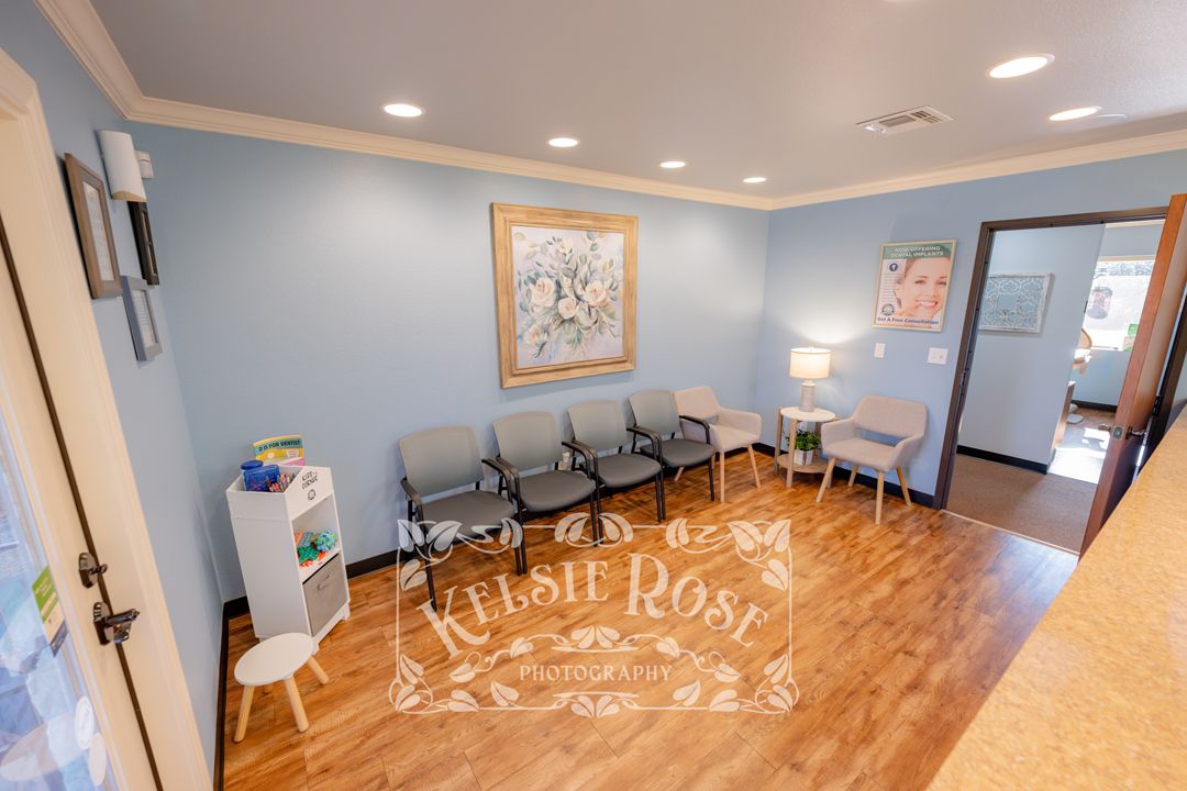 Spacious dental waiting area with blue walls, gray seating chairs, and hardwood floors.