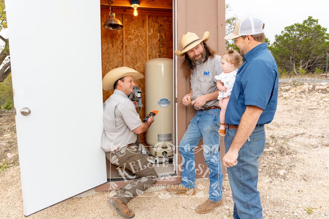 Two technicians in cowboy hats showing an installation in a well building to a couple with a baby.