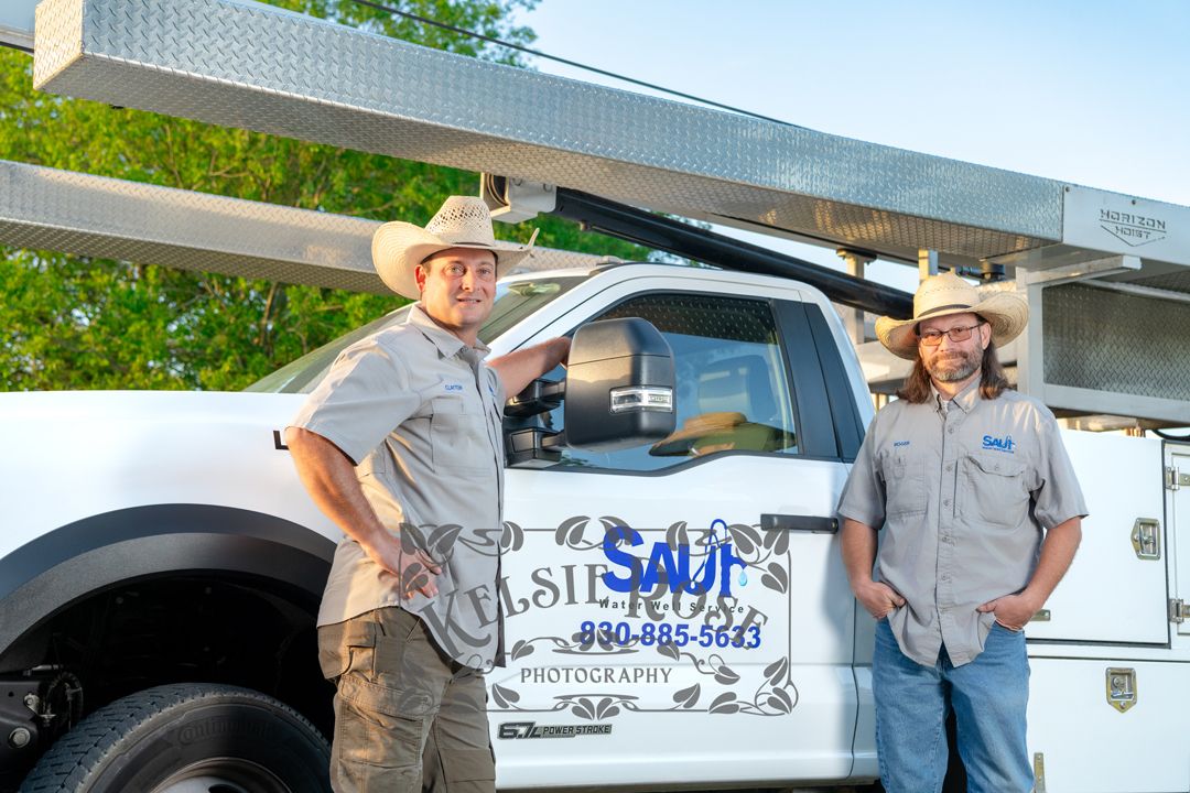 Two Saul Water Well Service technicians in cowboy hats posing beside company service truck.