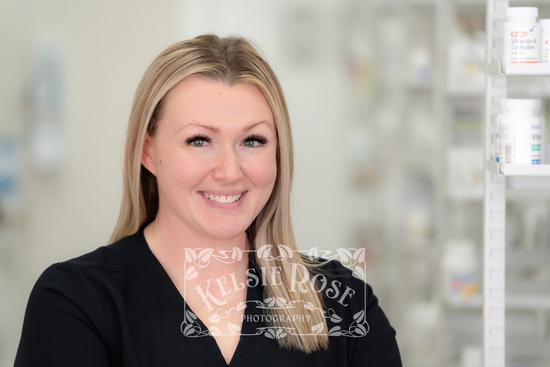 Headshot a smiling blonde female pharmacy technician in black scrubs inside a pharmacy.