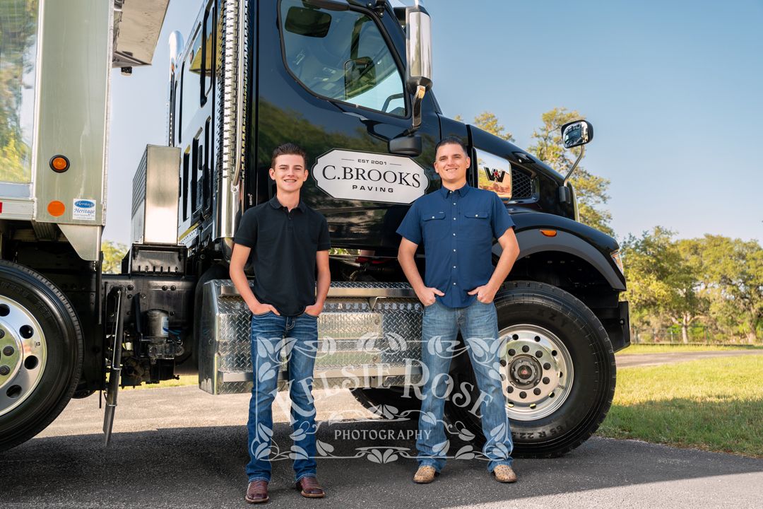 Two men standing confidently in front of a C. Brooks Paving company truck outdoors.