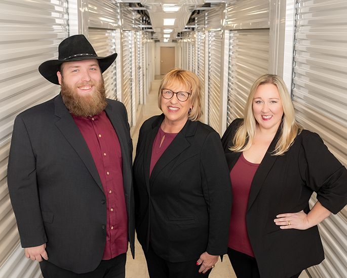 Three professionals in black blazers pose confidently in a storage facility hallway.