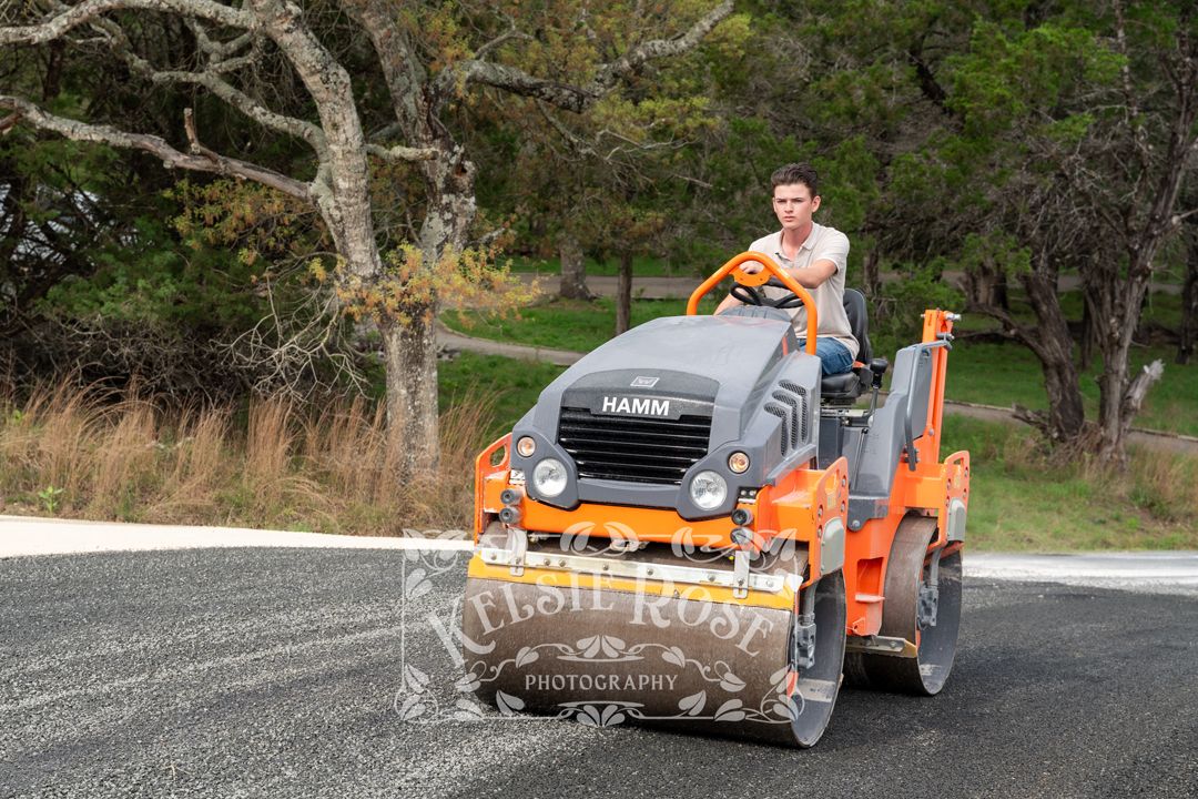 Young man operating an orange steamroller on a newly paved road.