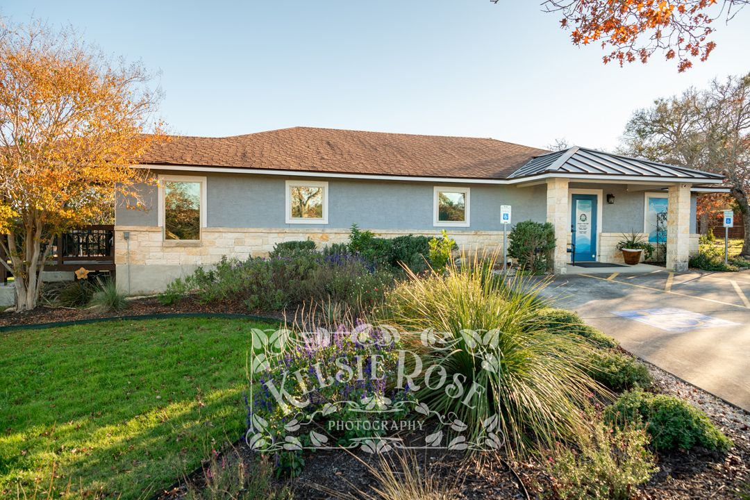 Front view of a dental practice with blue door with lush green lawn, and colorful autumn foliage trees.