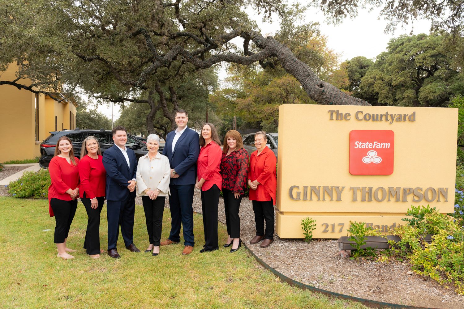 State Farm agent Ginny Thompson and her team pose outdoors at next to office sign in a professional group photo.
