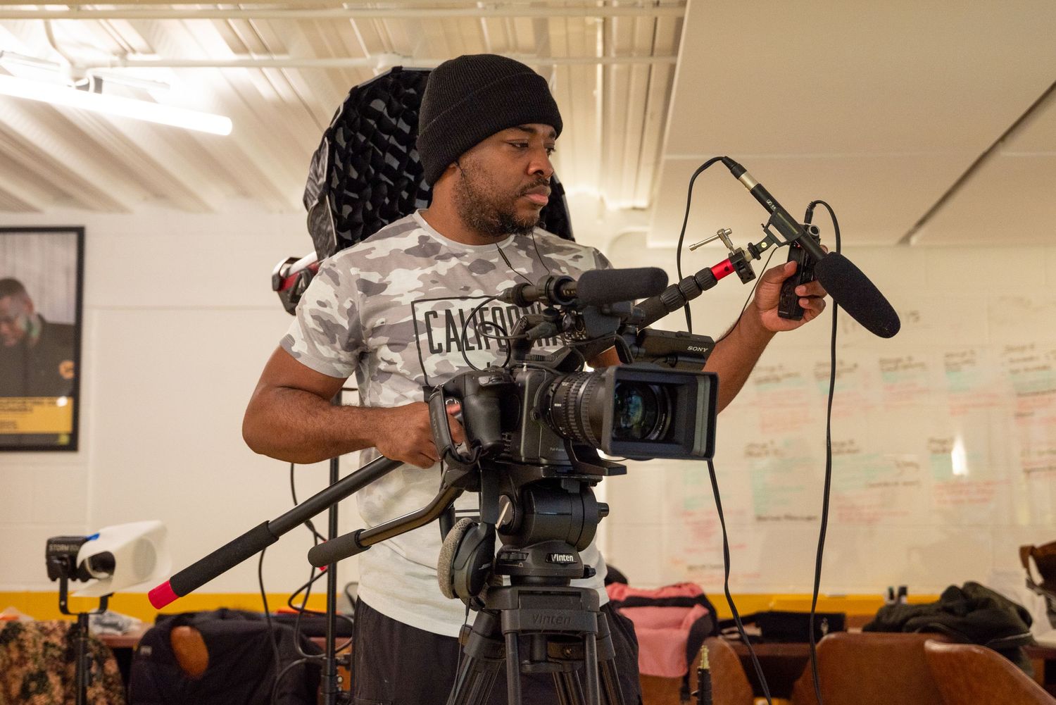 Professional camera operators film a scene in a bright indoor studio space with lighting and equipment visible.