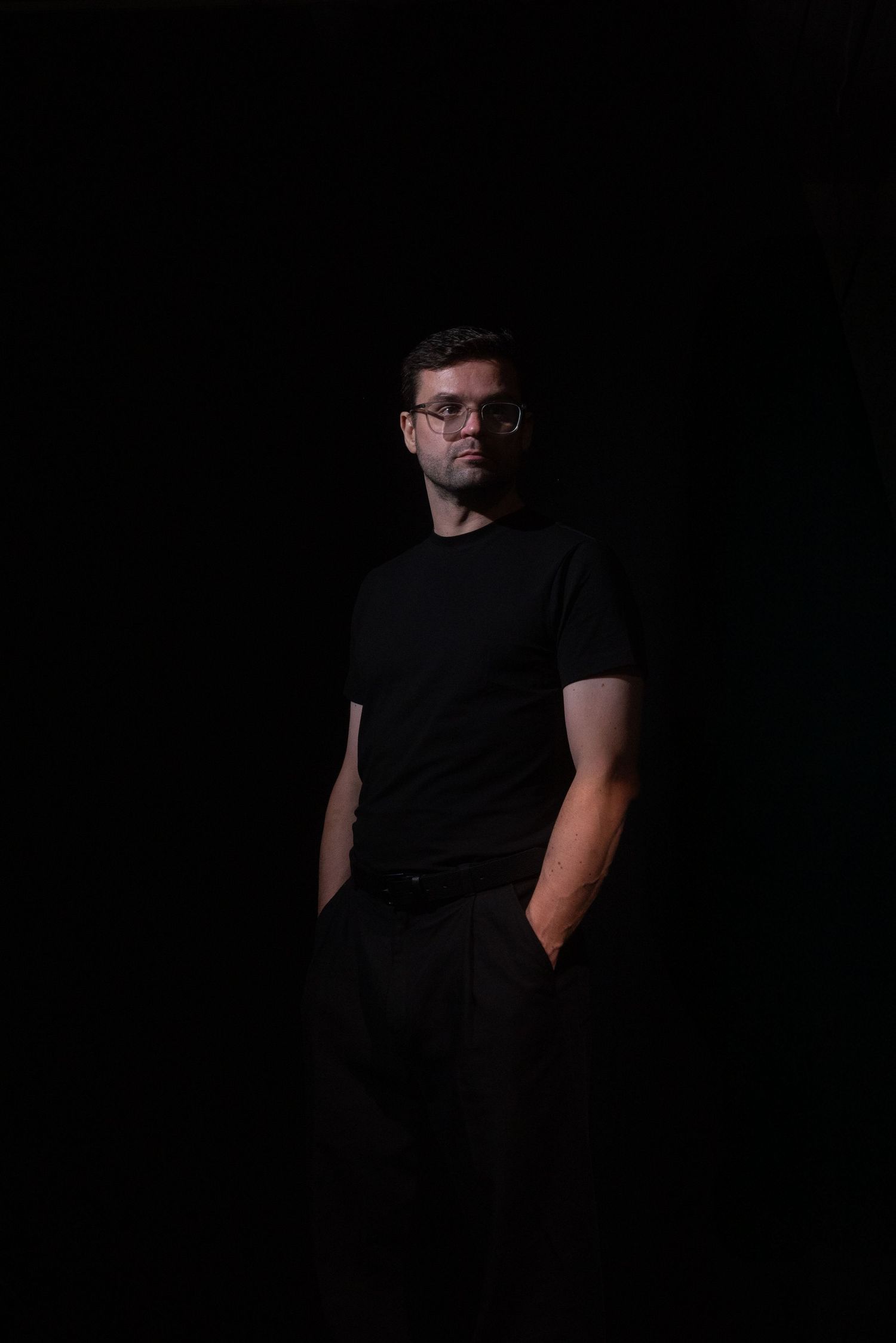 Dark artistic portrait of someone wearing black clothing against a black background creating a dramatic silhouette effect.