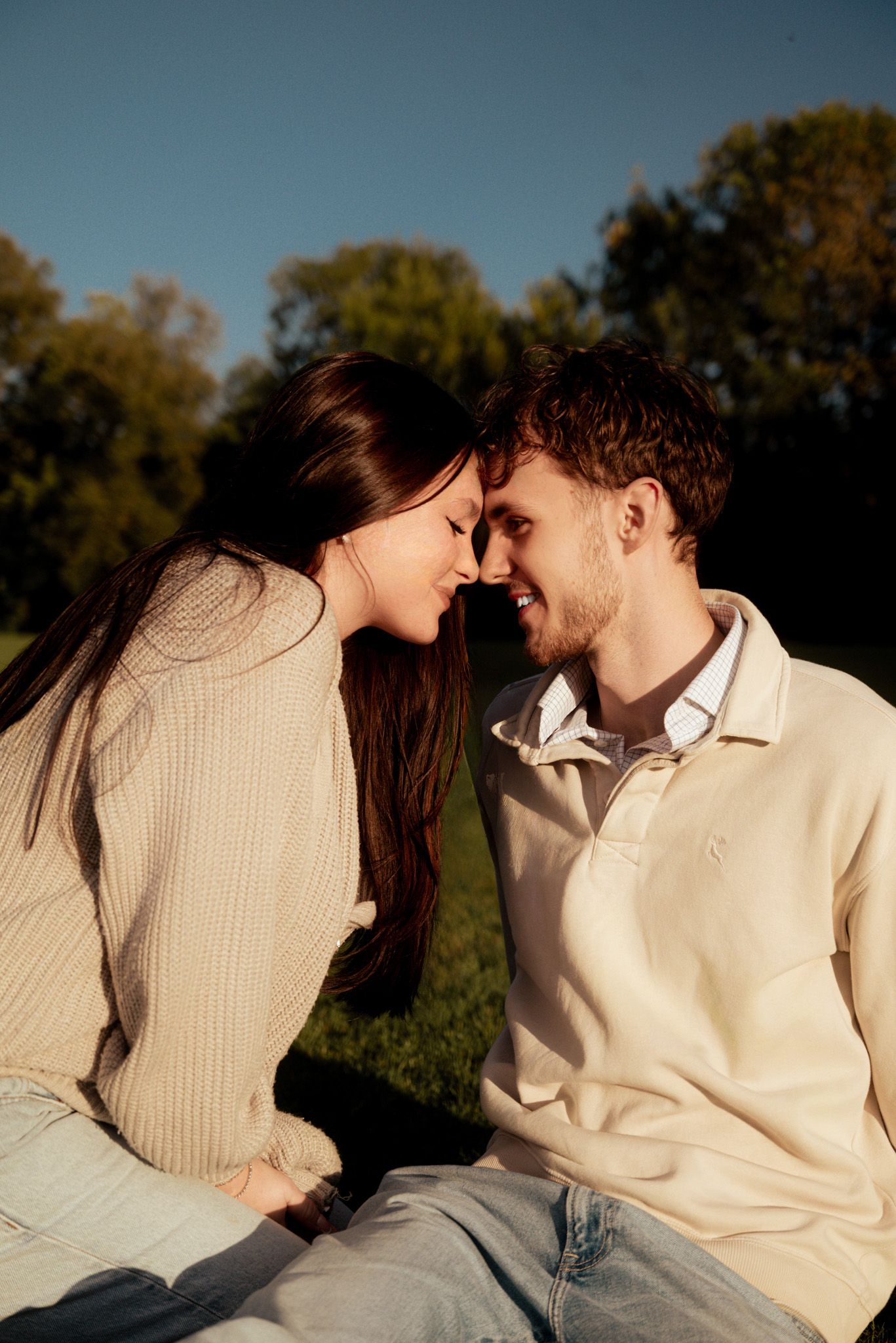 Romantic couple in beige sweaters sharing intimate moment outdoors during golden hour.