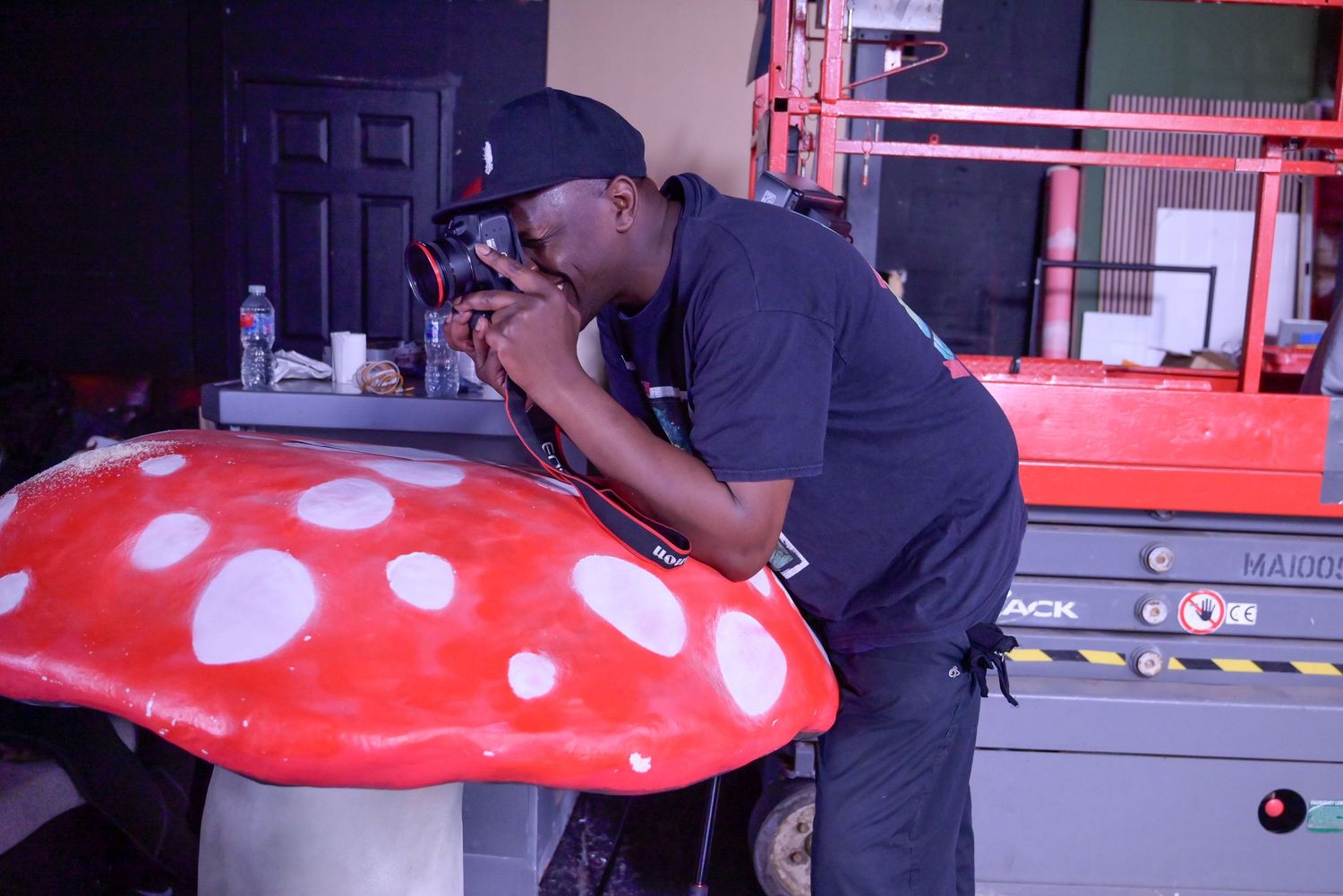 Film crew working with large red mushroom prop on studio set.