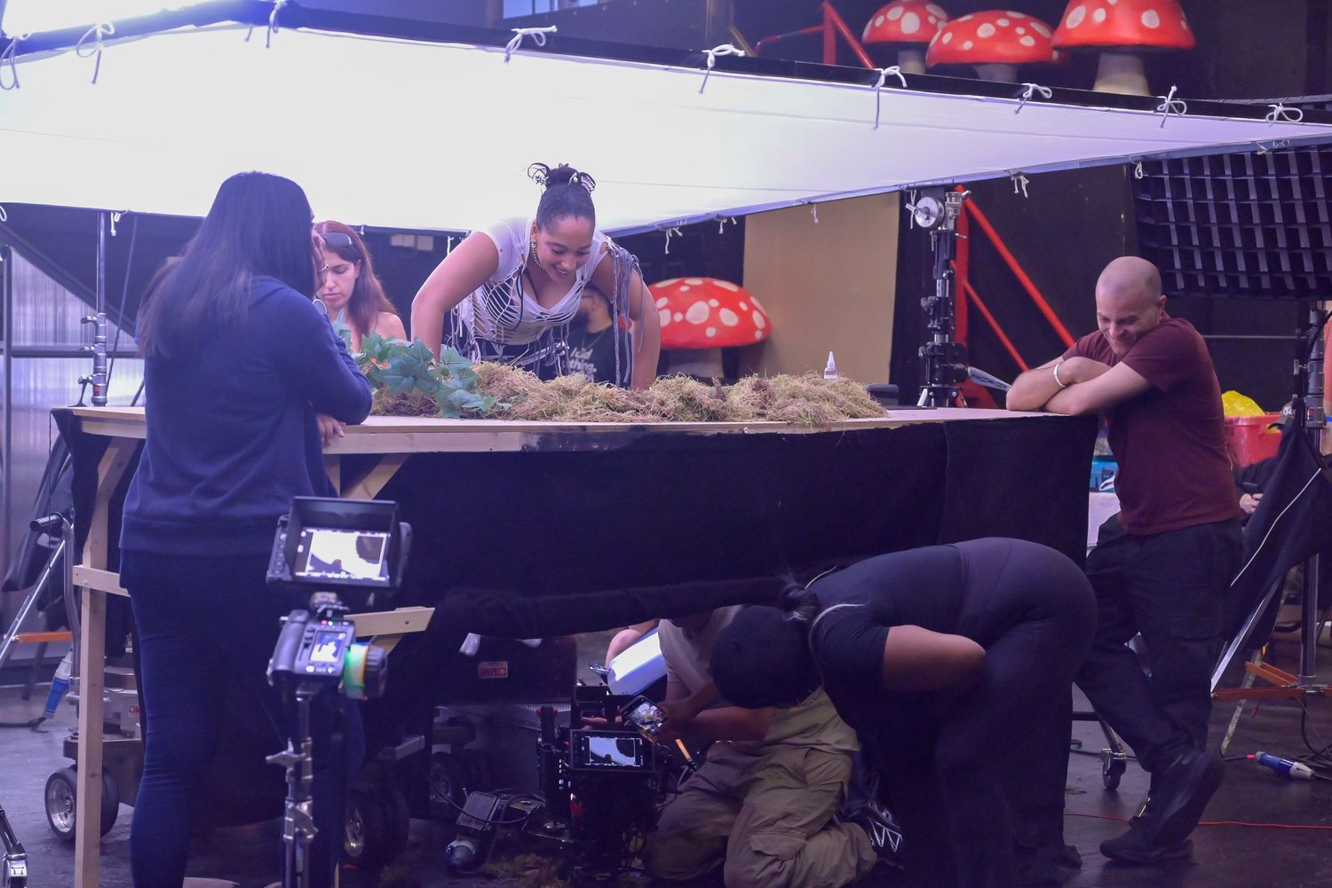 Production team collaborates around table setup with red mushroom props on film set.