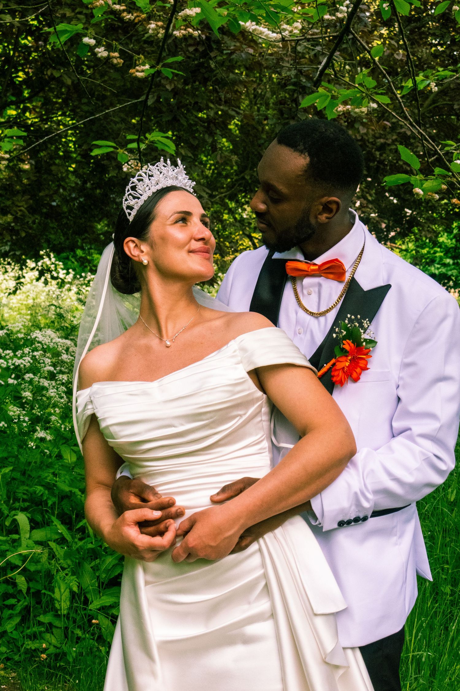 A romantic wedding photoshoot in a lush green garden setting with the couple embracing in formal attire.