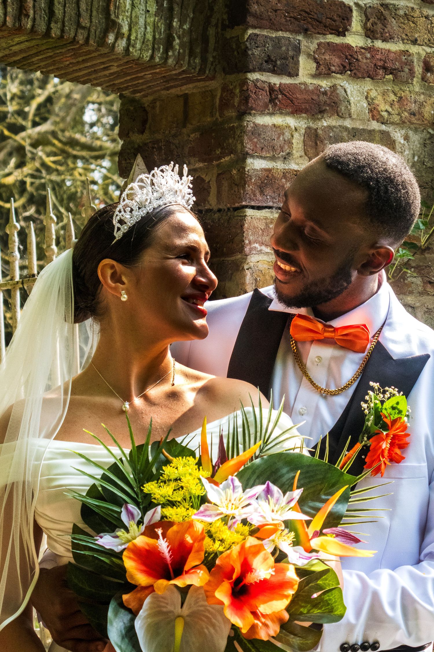 A vibrant wedding portrait with the bride holding a colorful tropical bouquet next to a brick wall.