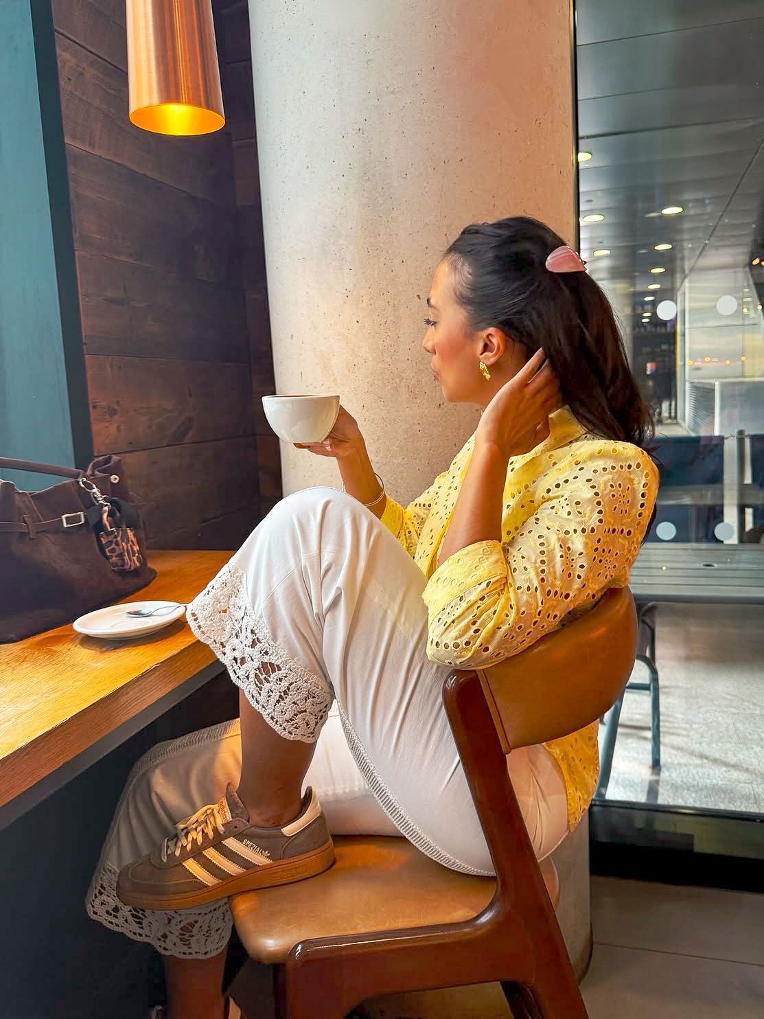 Person in white and yellow attire sitting by a modern window with warm lighting.
