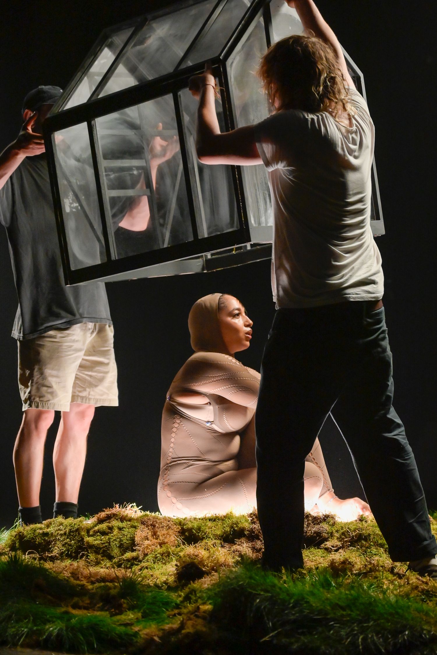 Artists working on arranging a glass greenhouse installation in dramatic lighting.