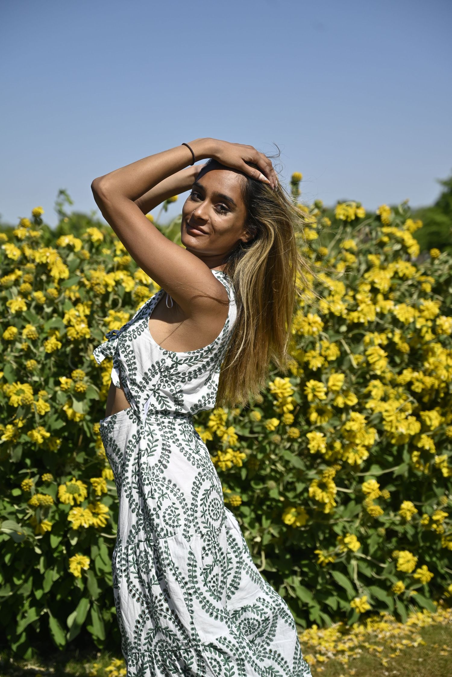 White patterned sundress flowing in a field of bright yellow sunflowers under blue sky.