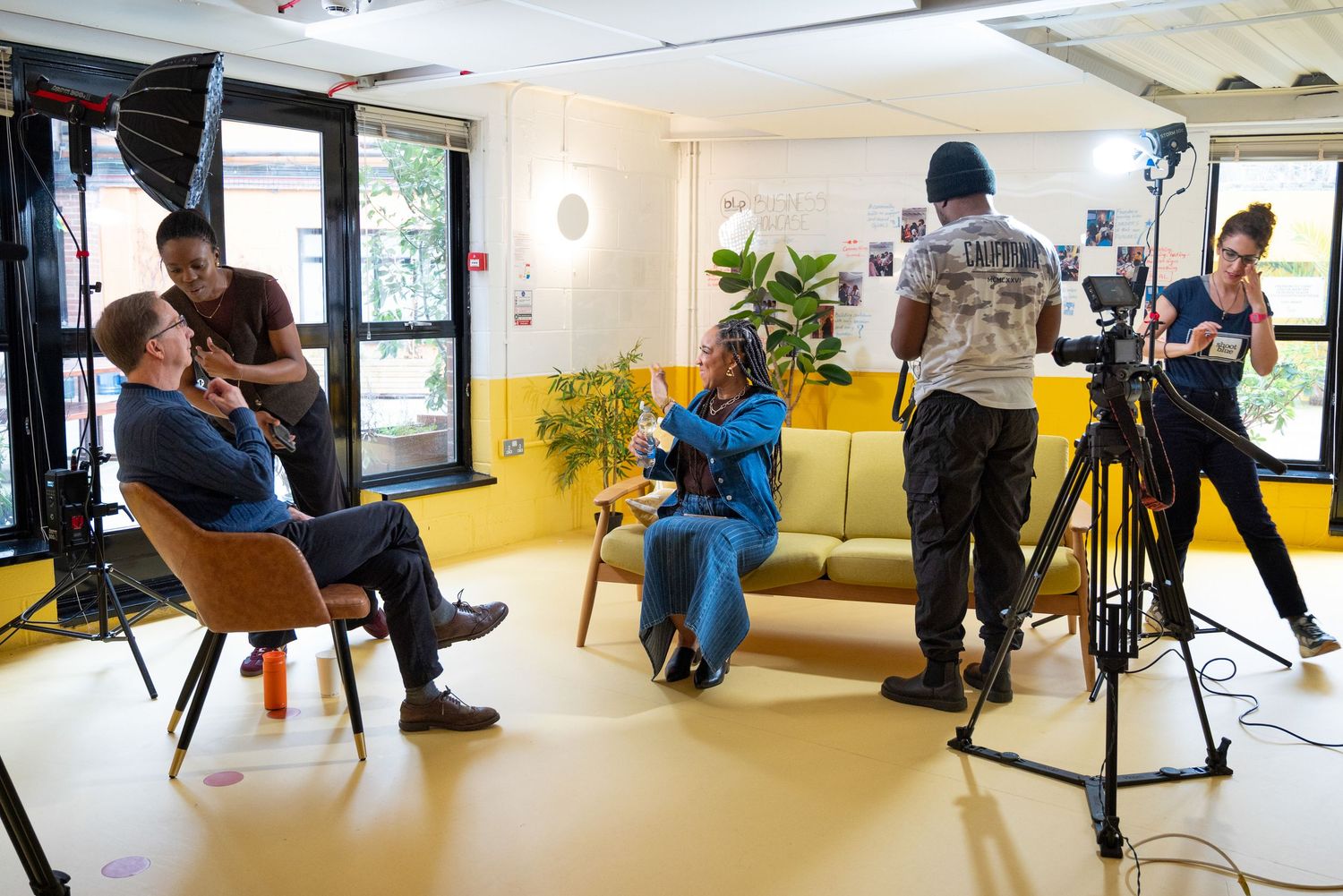 Professional photographers and crew set up lighting and camera equipment in a bright studio space for a photo shoot.