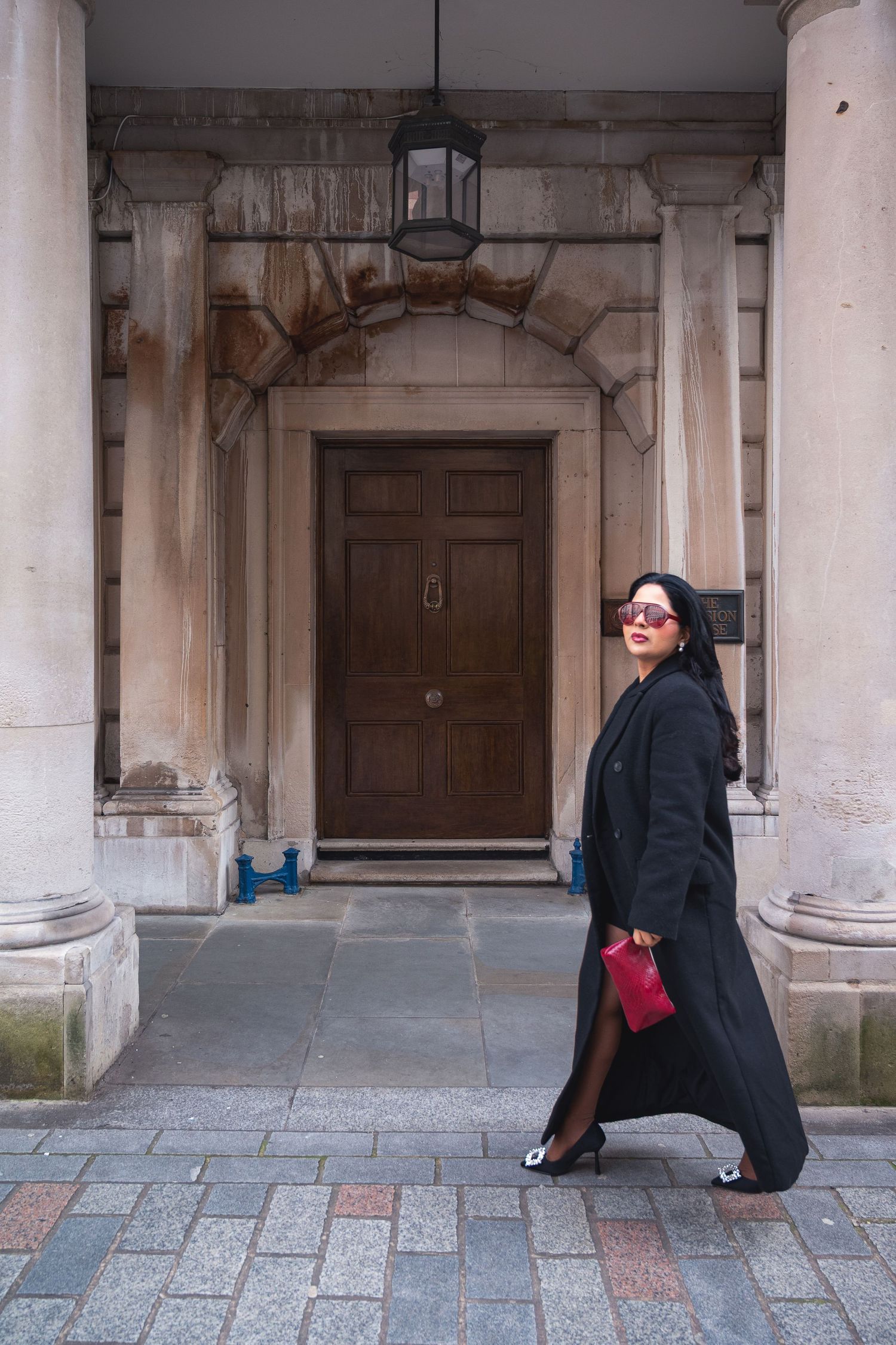 A person in black clothing crouches on a stone floor in a classical colonnade with arched doorways and pillars.