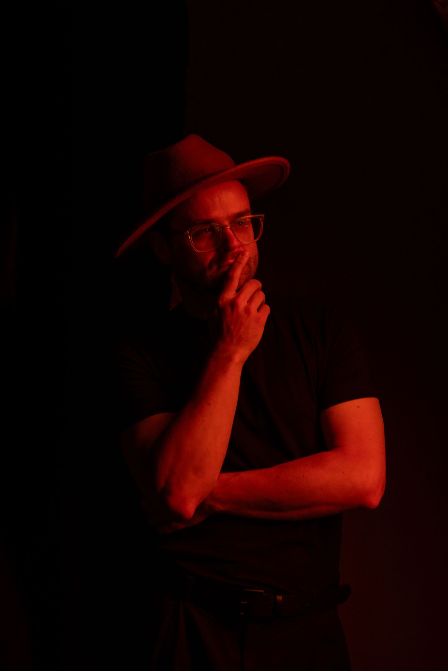 A series of dark silhouettes against a red background showing someone adjusting a hat in dramatic lighting.