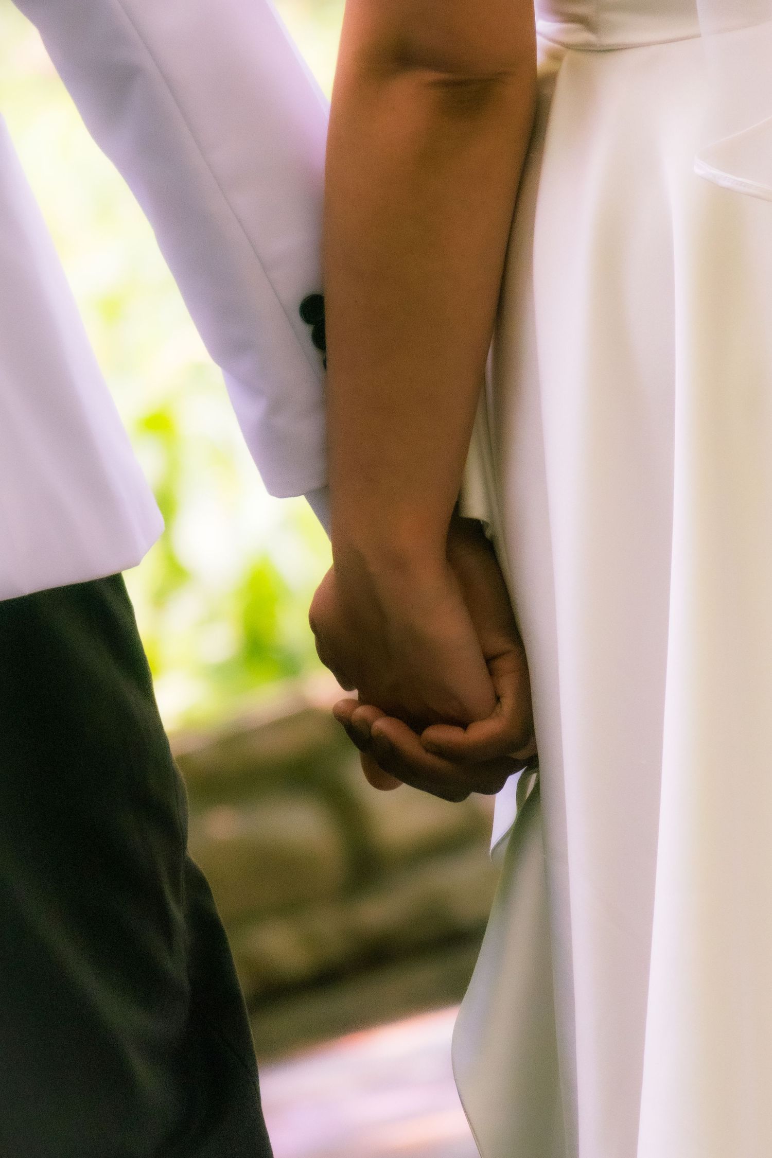 Close-up of a couple holding hands, showing the bride's white dress and groom's suit.