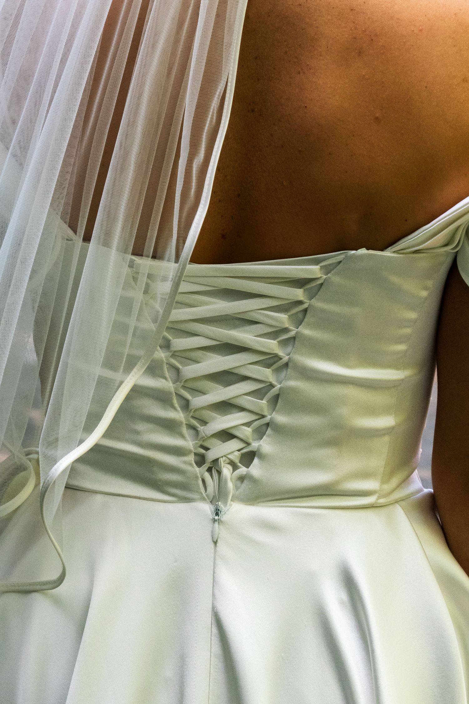 Close-up detail of a white satin wedding dress showing intricate corset-style lacing on the back.