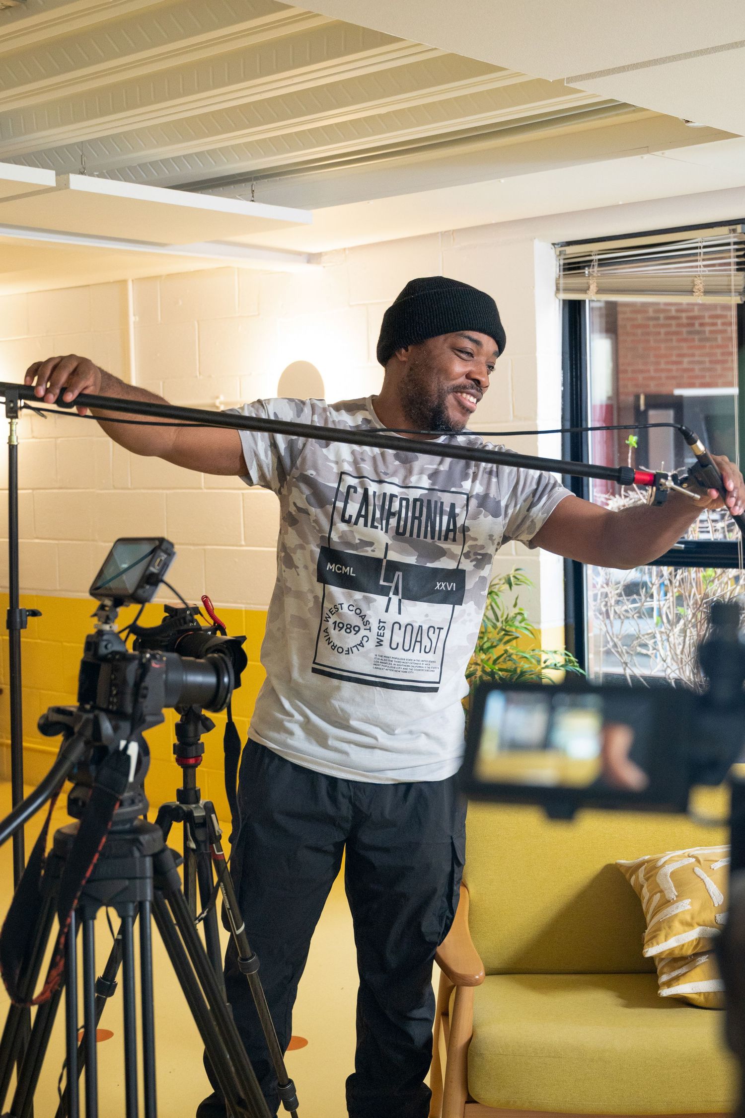 Person in a California t-shirt stretches with exercise bands in a home gym setup with camera equipment nearby.
