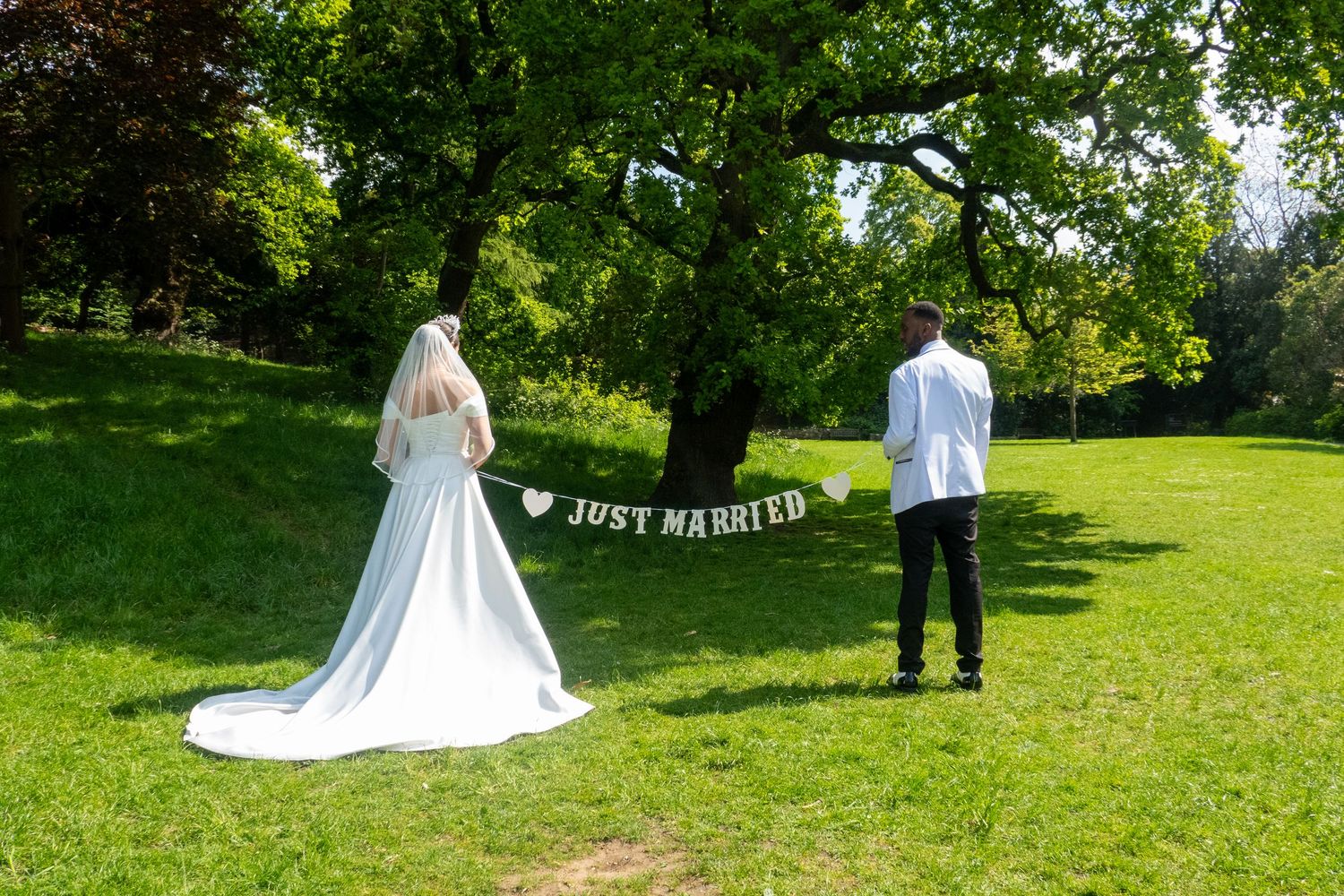 A couple stands in a garden with a 'Just Married' banner hanging between them.
