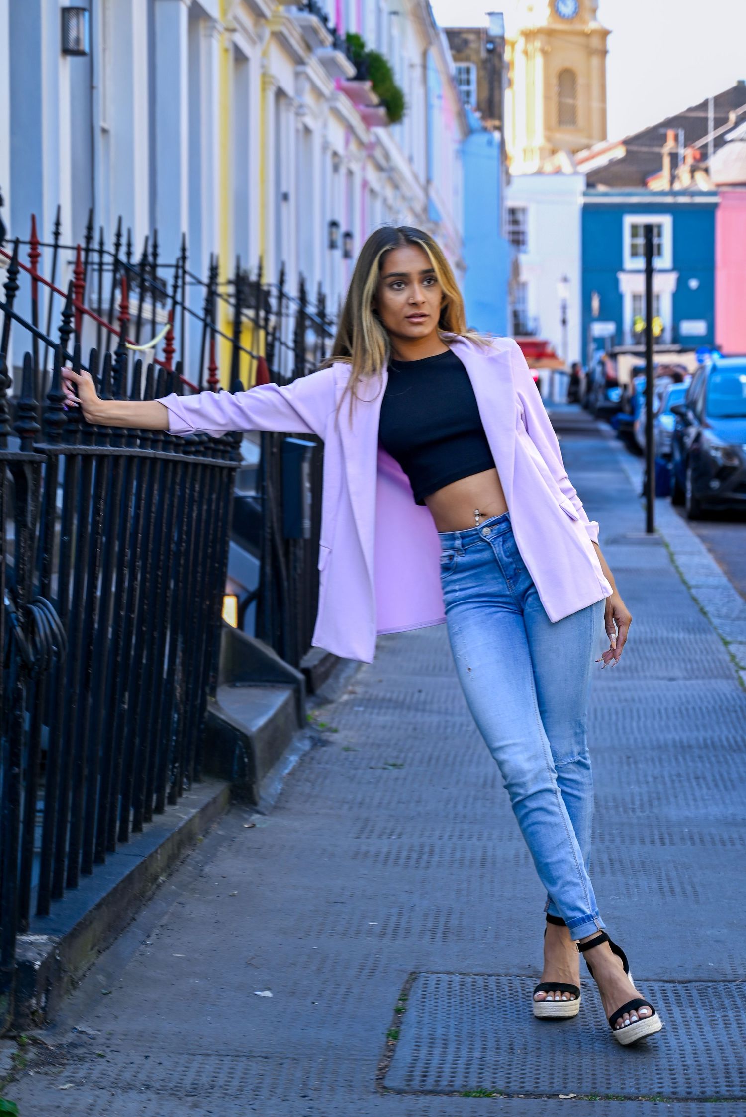 Person walking down a city street wearing light blue jeans and carrying a pink shopping bag.