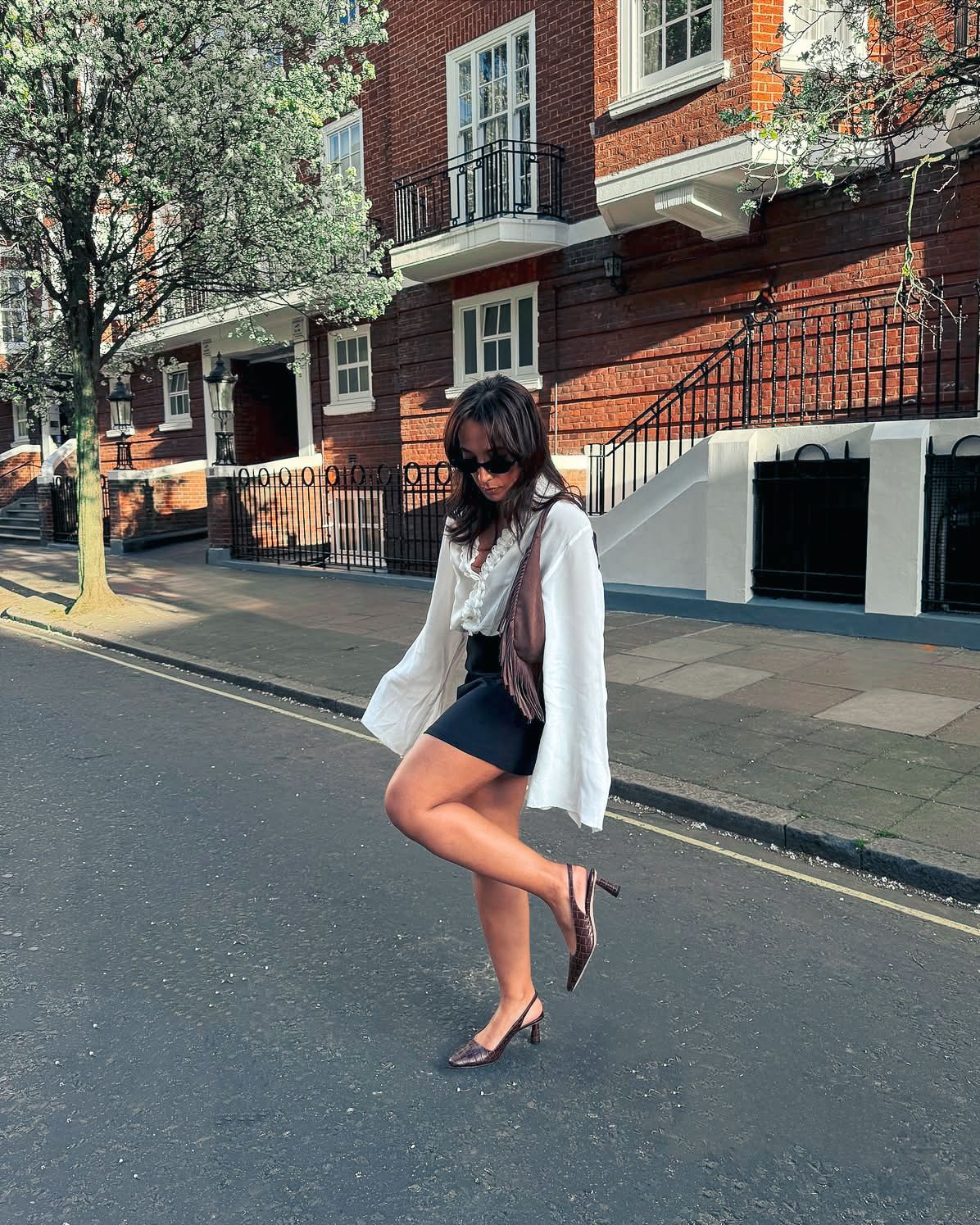 Figure in white top and dark skirt walking down a sloped brick street.