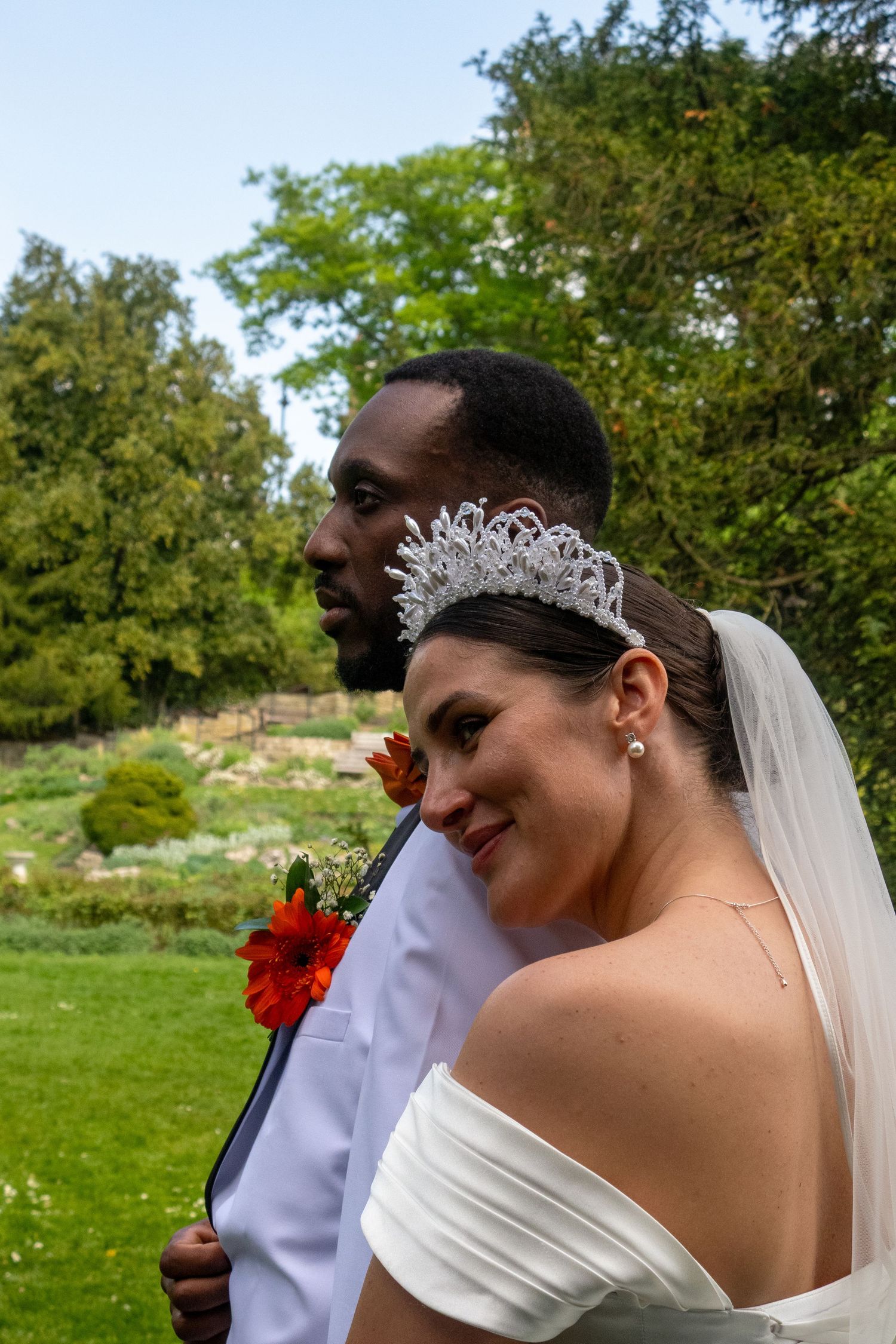 A joyful wedding couple shares a candid moment outdoors against a natural garden backdrop.