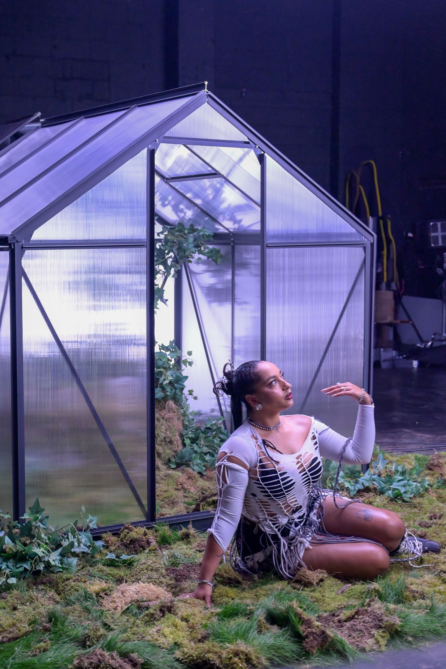 Artistic performance scene being filmed in front of illuminated greenhouse set.