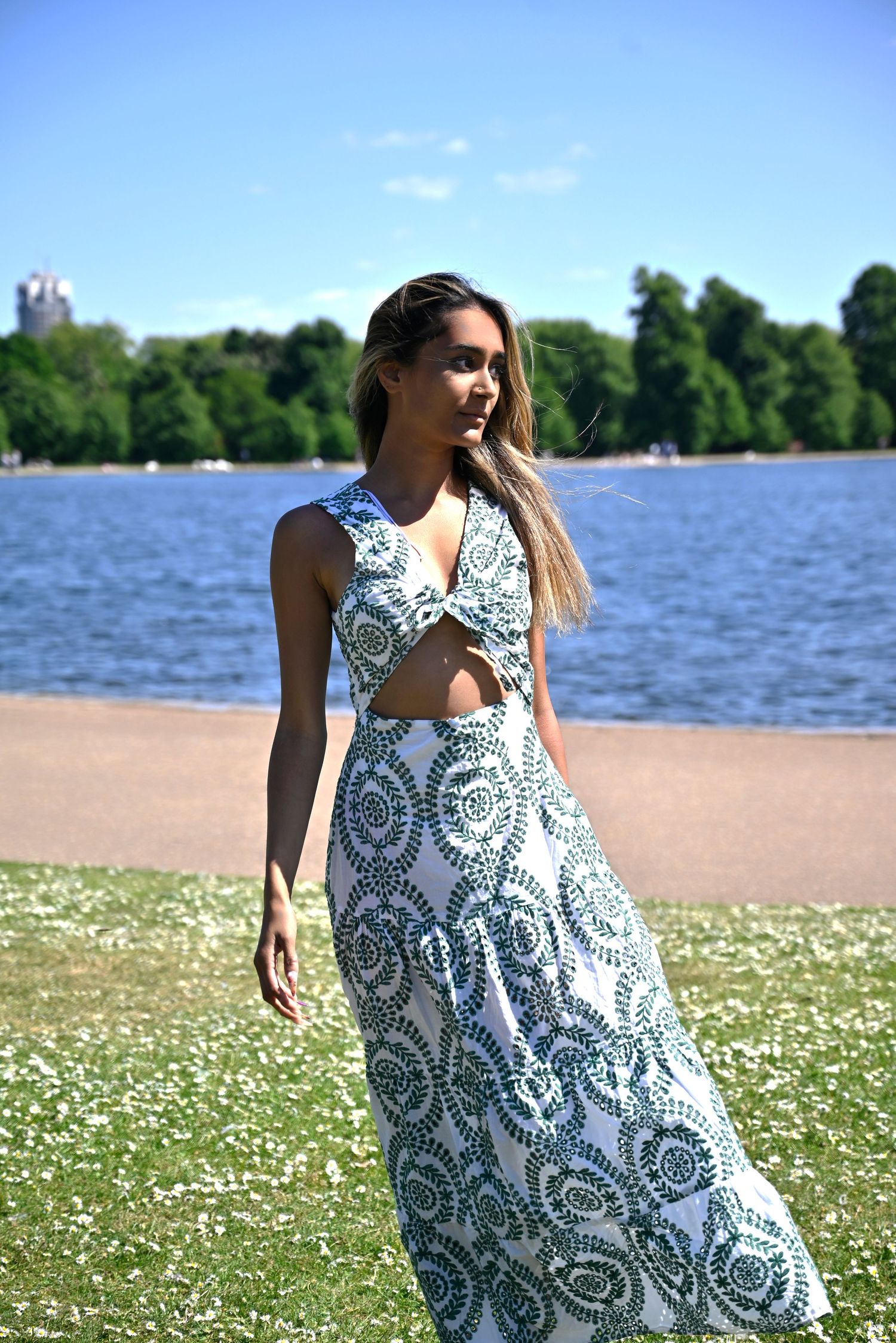 White lace dress flowing gracefully by a lakeside beach with daisies in foreground.