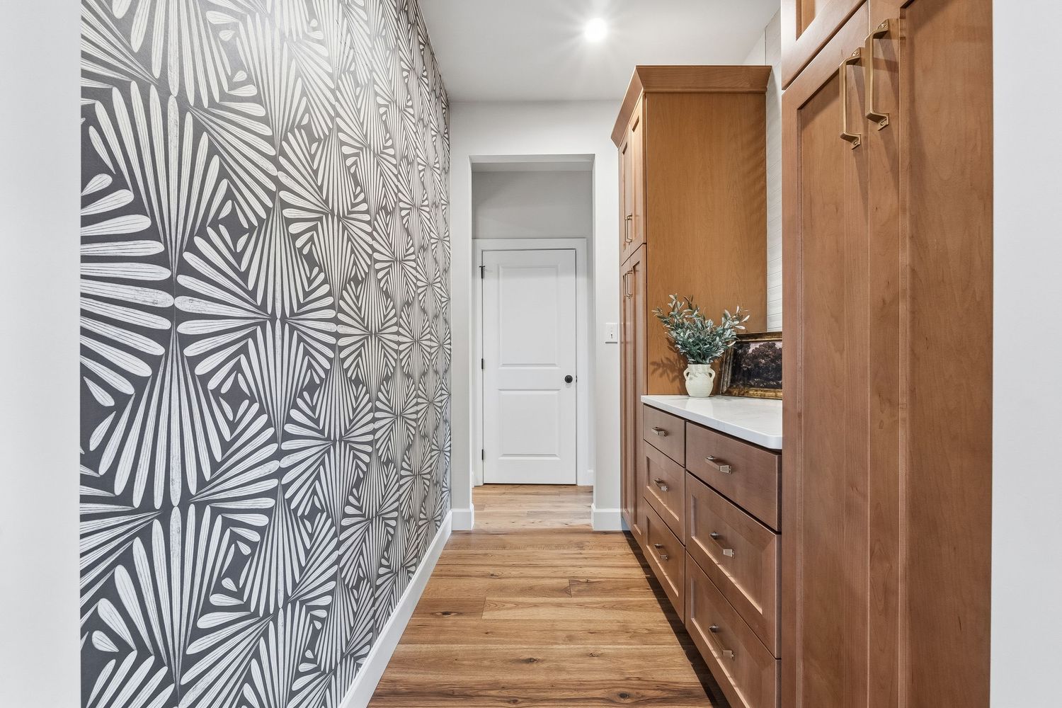 Custom hallway with patterned accent wallpaper, built-in wood cabinetry, and hardwood flooring, photographed for residential real estate lis