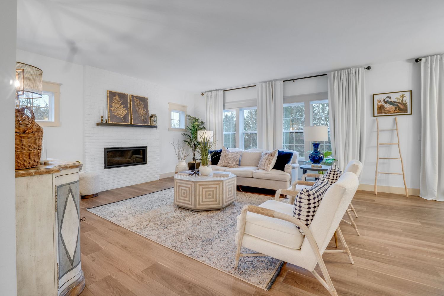 Bright living room with fireplace, modern furniture, large windows, and hardwood flooring, photographed for residential real estate
