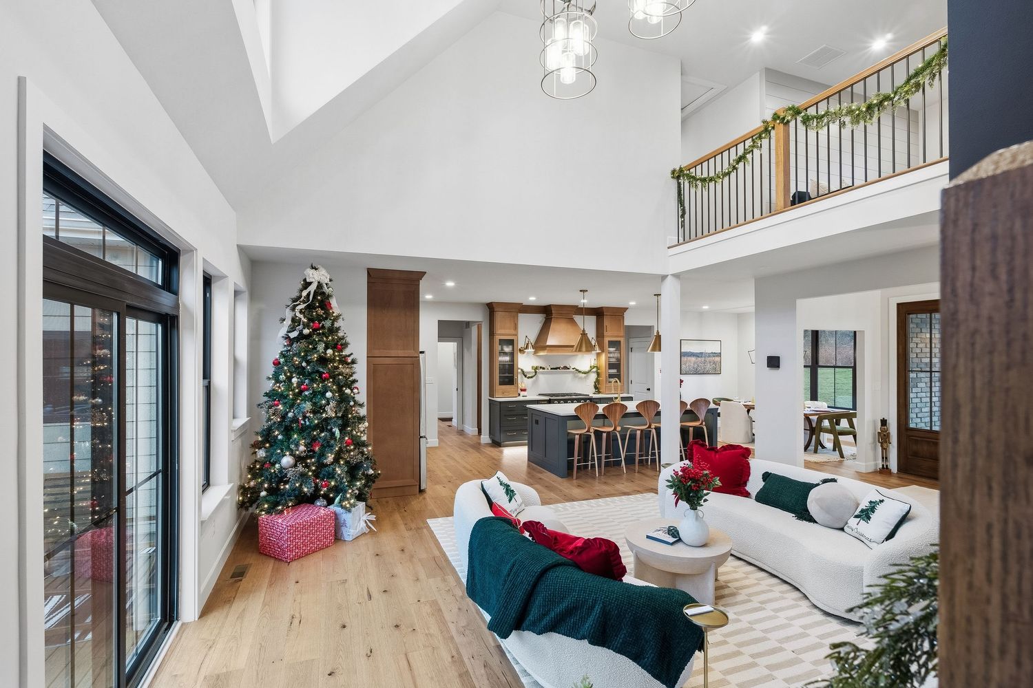 Open-concept living area with vaulted ceiling, hardwood flooring, large windows, and kitchen in background, photographed for real estate mar