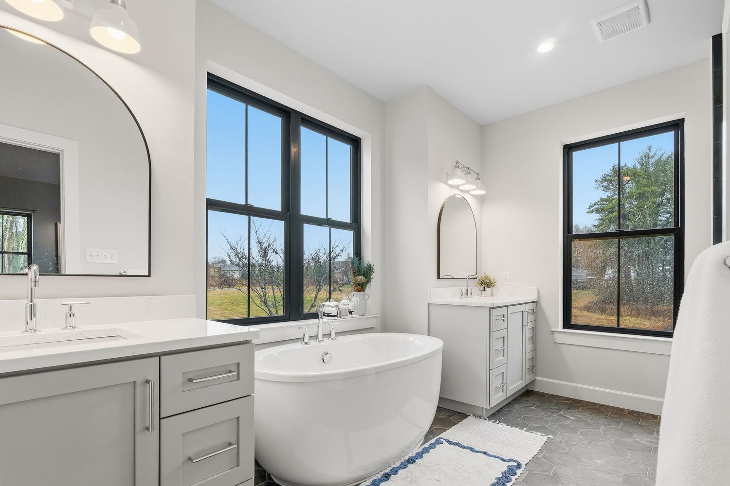 Modern bathroom with freestanding soaking tub, double vanity, large windows, and natural light, photographed for real estate listing
