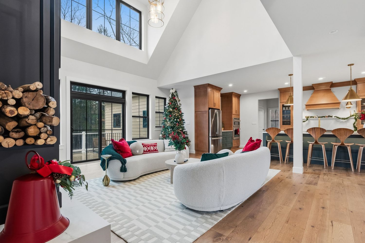 Open-concept living room with vaulted ceiling, large windows, hardwood floors, and adjacent kitchen, photographed for residential real estat