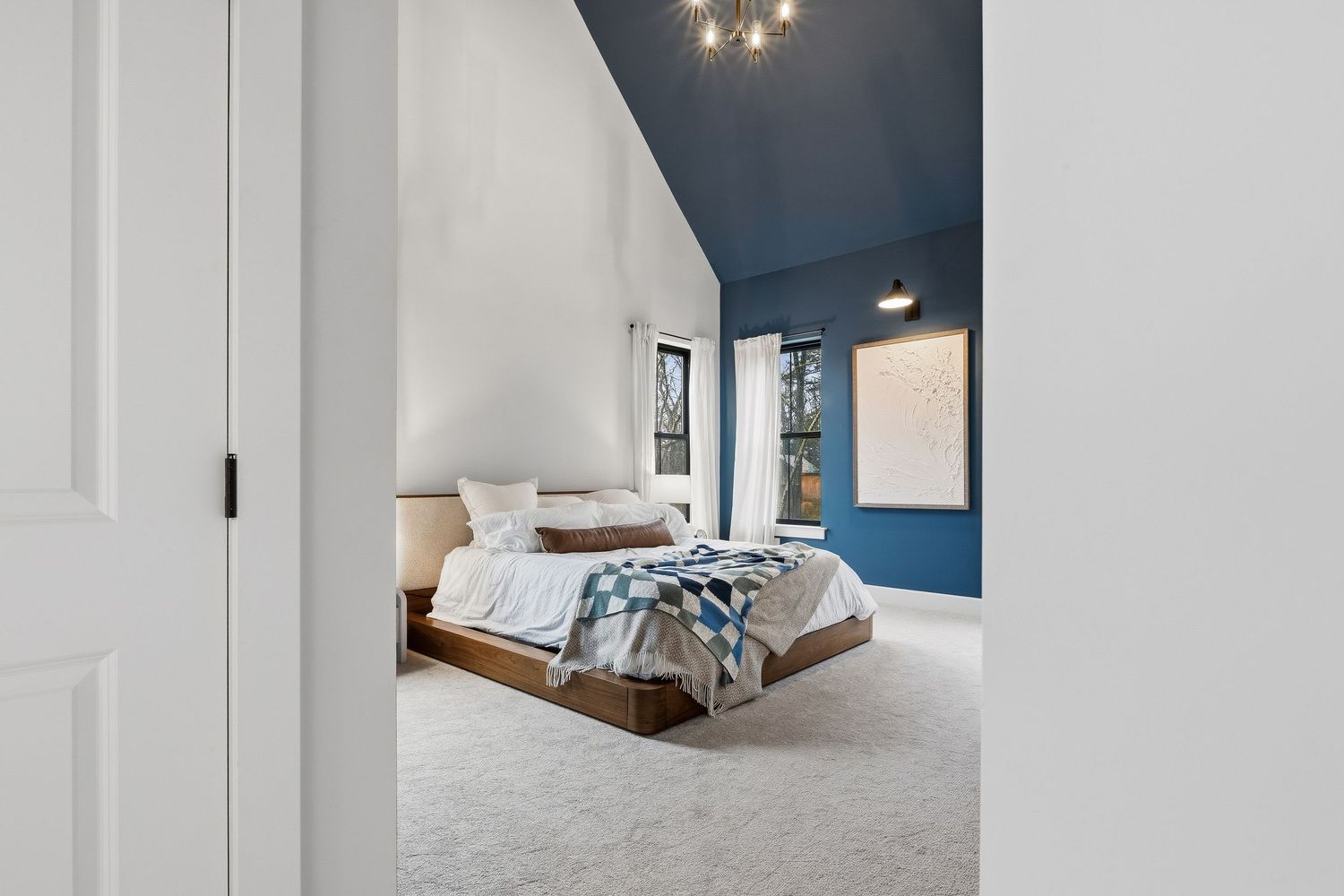 Primary bedroom with vaulted ceiling, blue accent wall, neutral carpet, and modern bed, photographed for real estate marketing