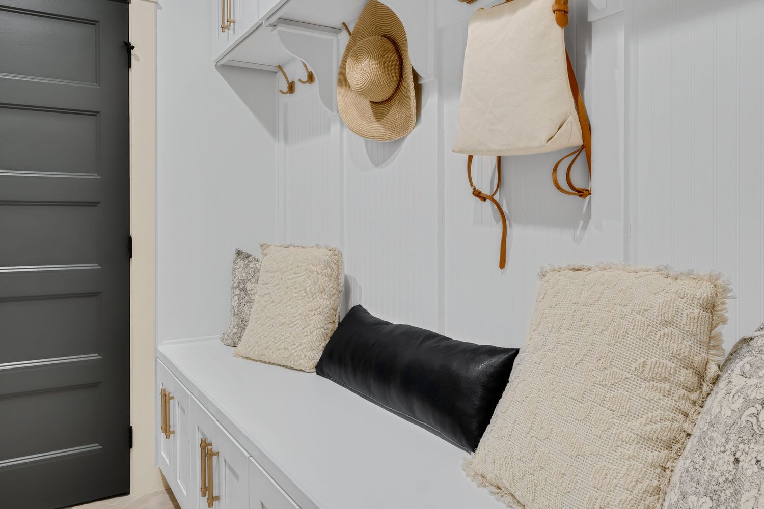 Built-in entryway bench with wall hooks, neutral pillows, and functional storage, photographed for real estate marketing