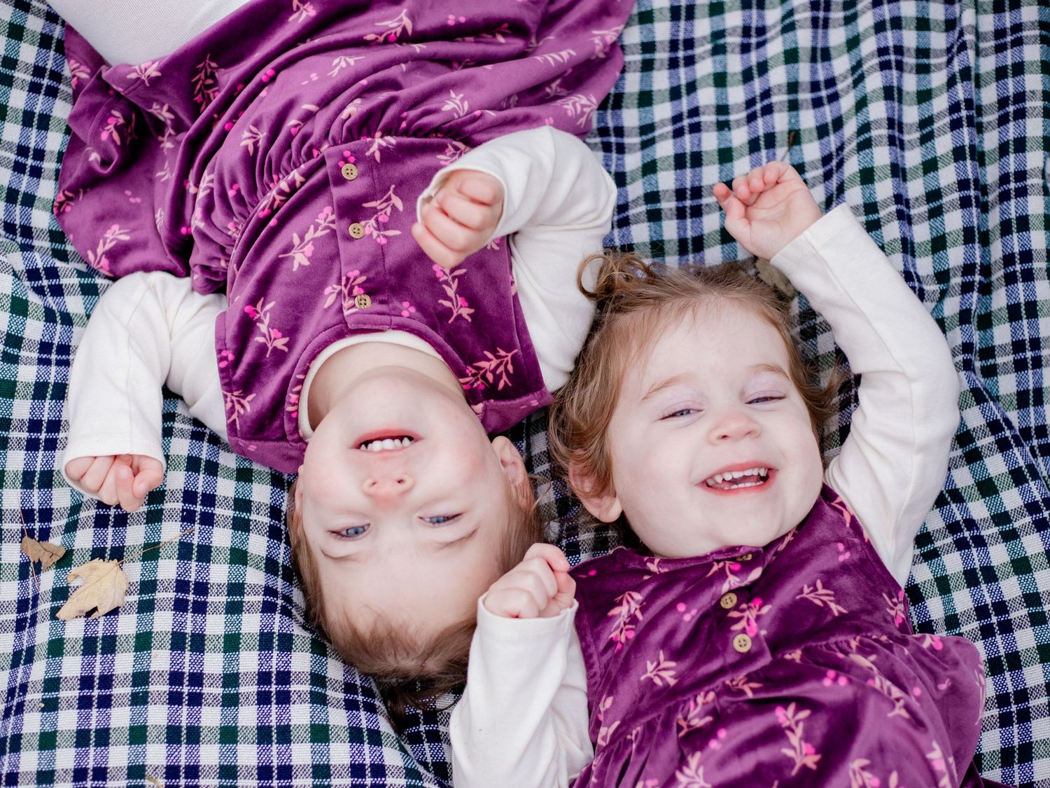 Photo of twin girls laying on a blanket smiling up at the camera