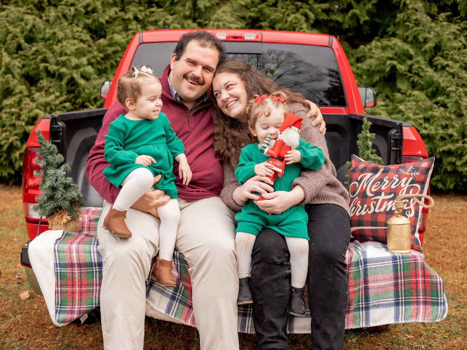 Mom and Dad with their twin girls sitting in the bed of their red pick up truck during a Christmas photo session in Harford County, MD