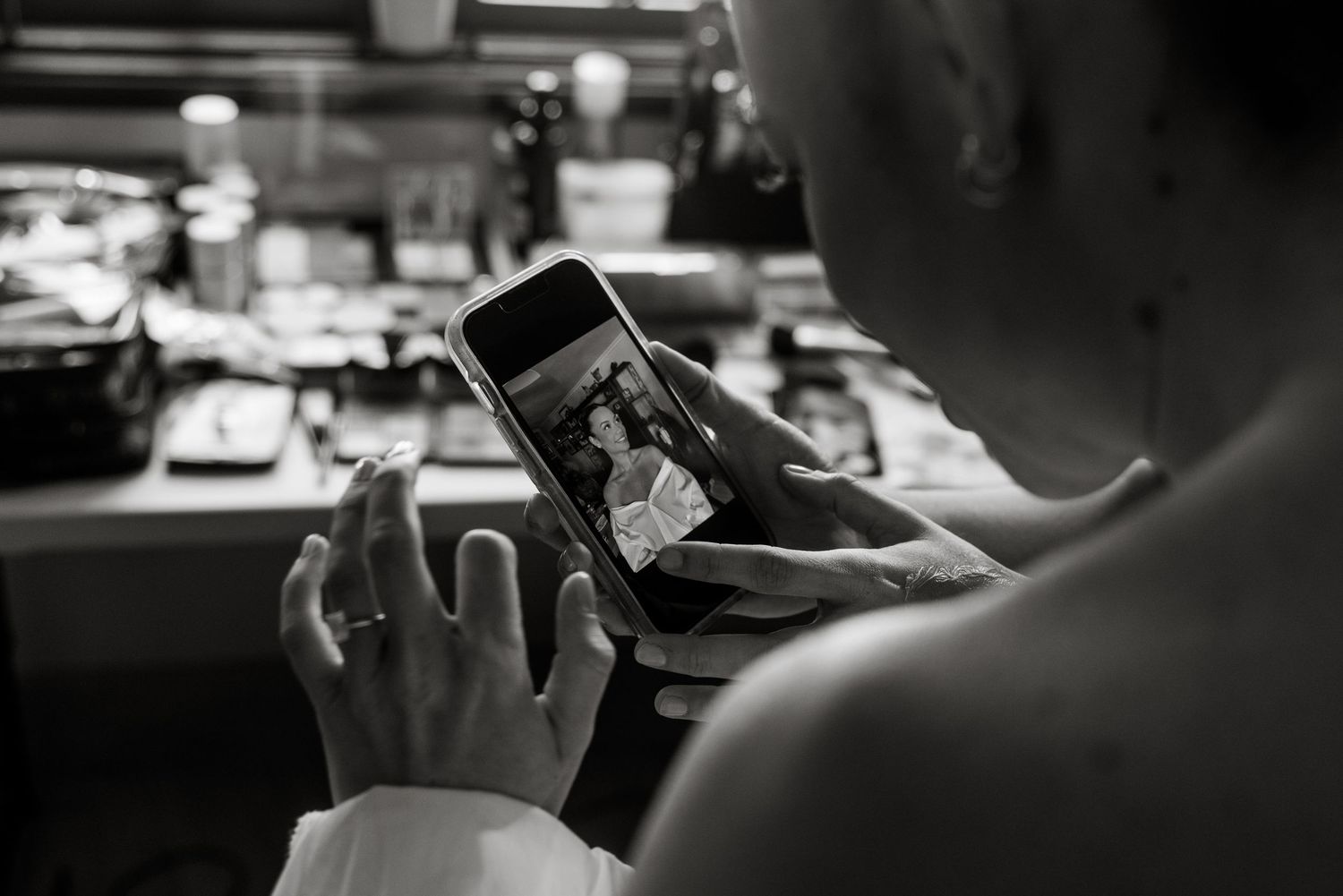 A bride views a wedding photo on her smartphone in black and white at a dressing table.