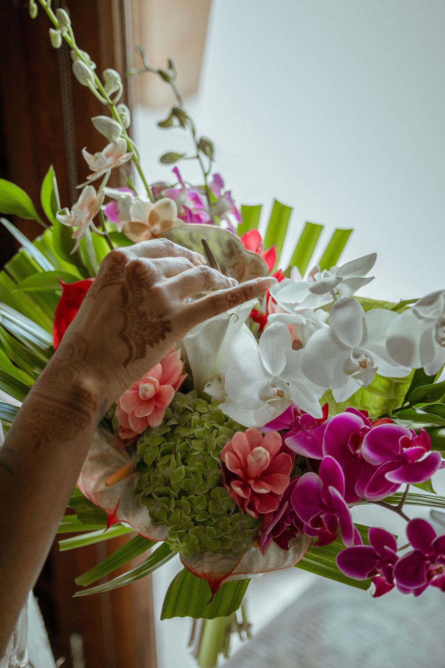 Hand with henna touching vibrant tropical bouquet of orchids and hydrangeas.