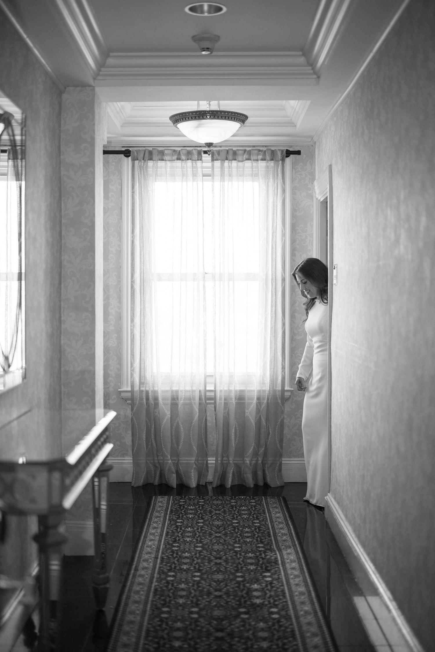 Peering from the hallway to Bride having a quiet moment leaving Boston hotel room on wait to her wedding.