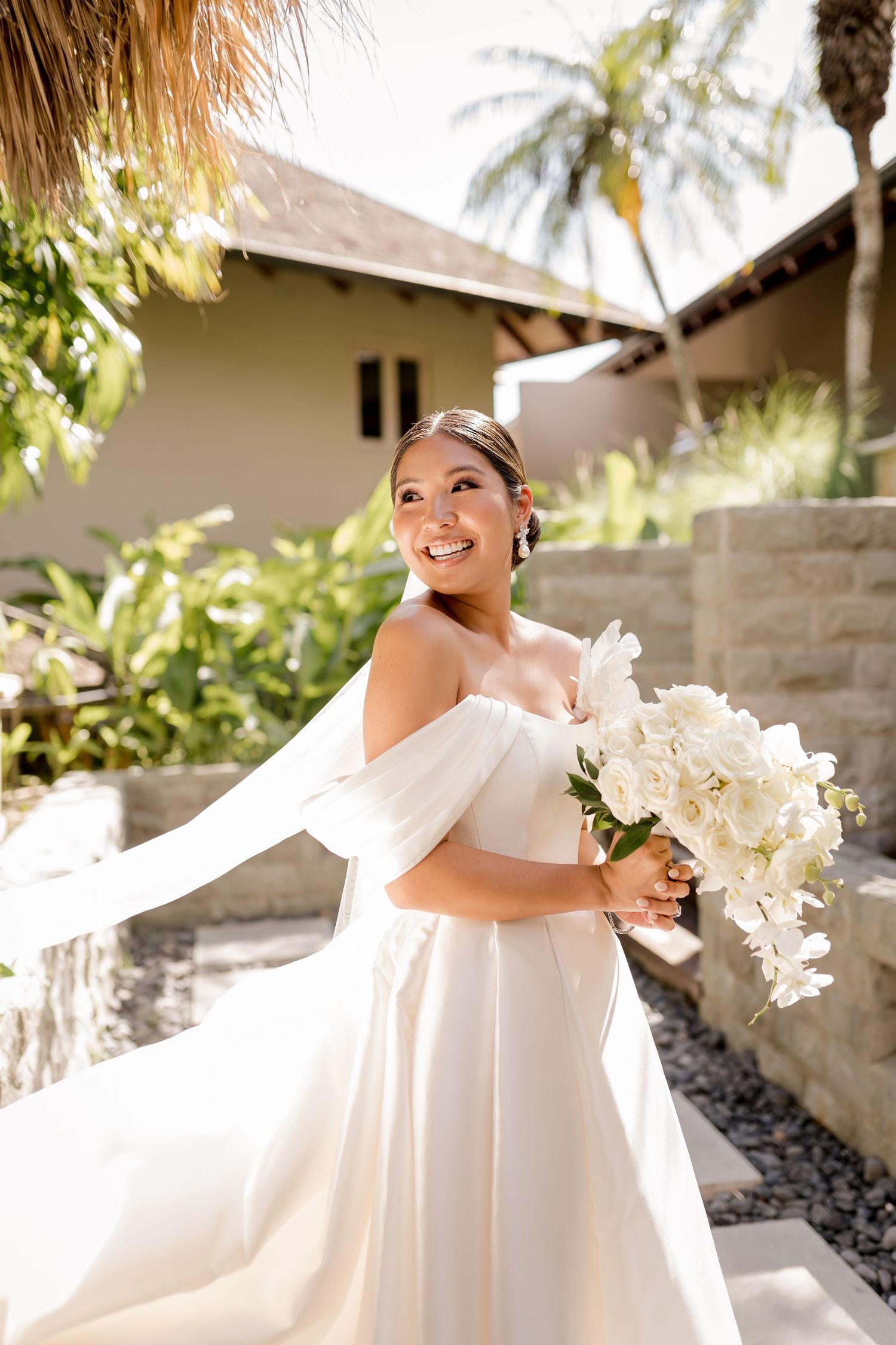 Editorial bridal portrait featuring flowing movement, tropical surroundings, and a cascading white orchid bouquet.