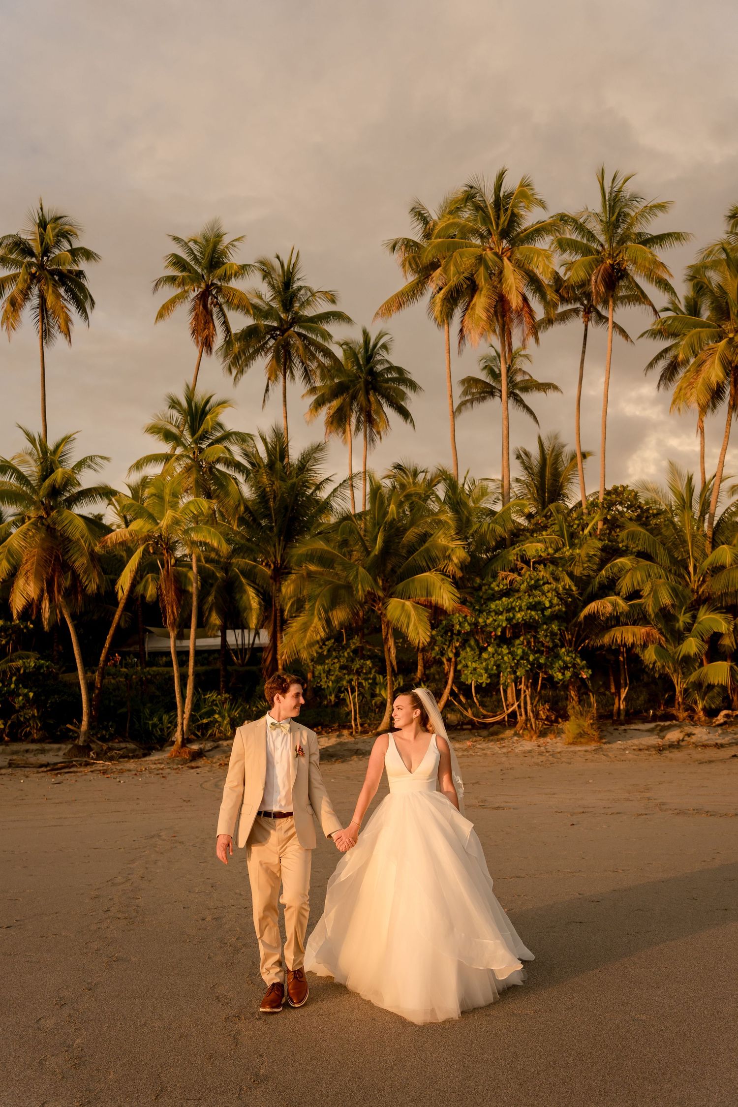 Newlyweds walking along a palm-lined beach during a luxury destination wedding on Costa Rica's Pacific coast.