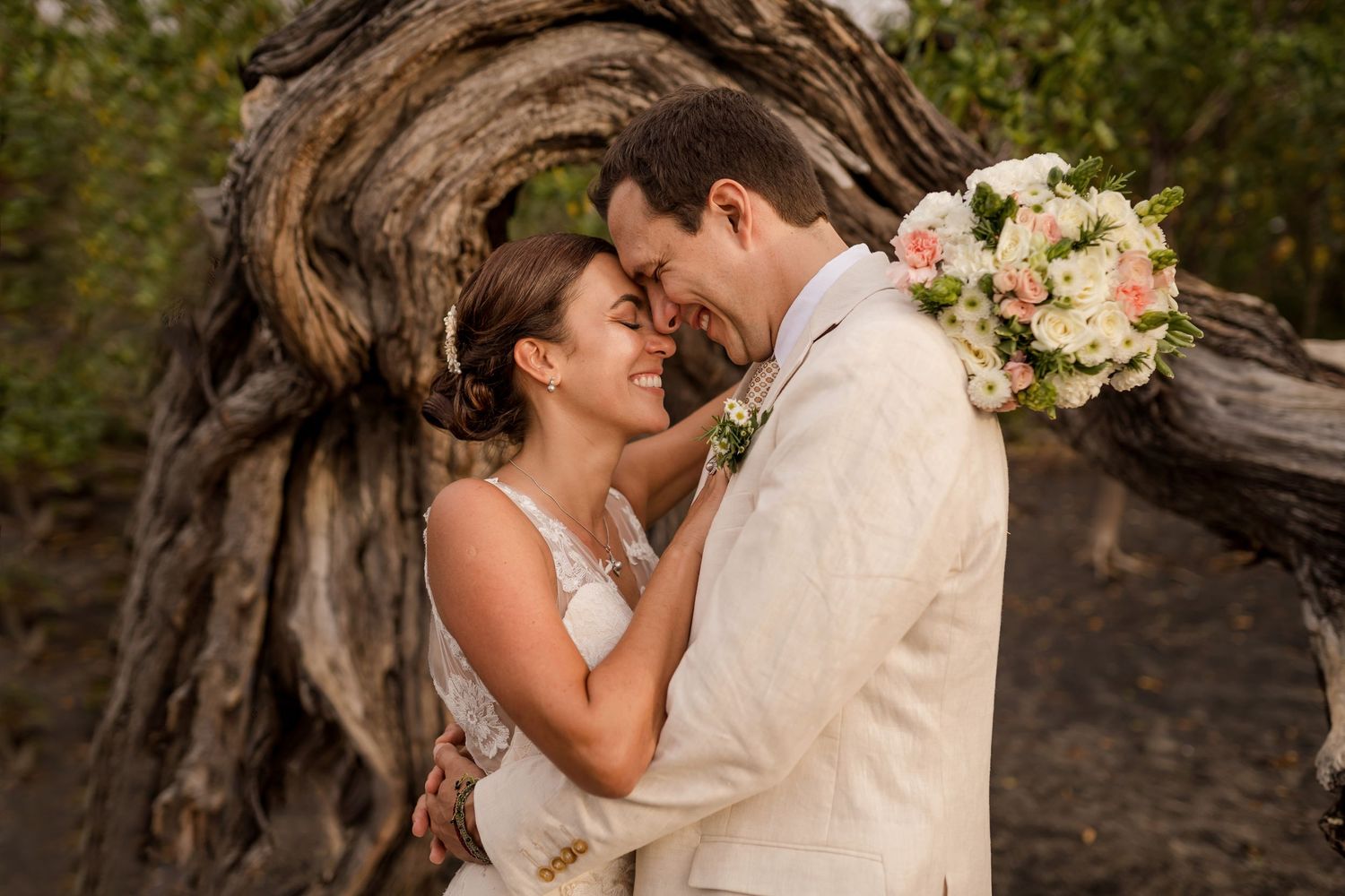Bride and groom sharing a romantic moment under a twisted driftwood arch, bride holding a pink and white bouquet in Ocotal, Costa Rica.