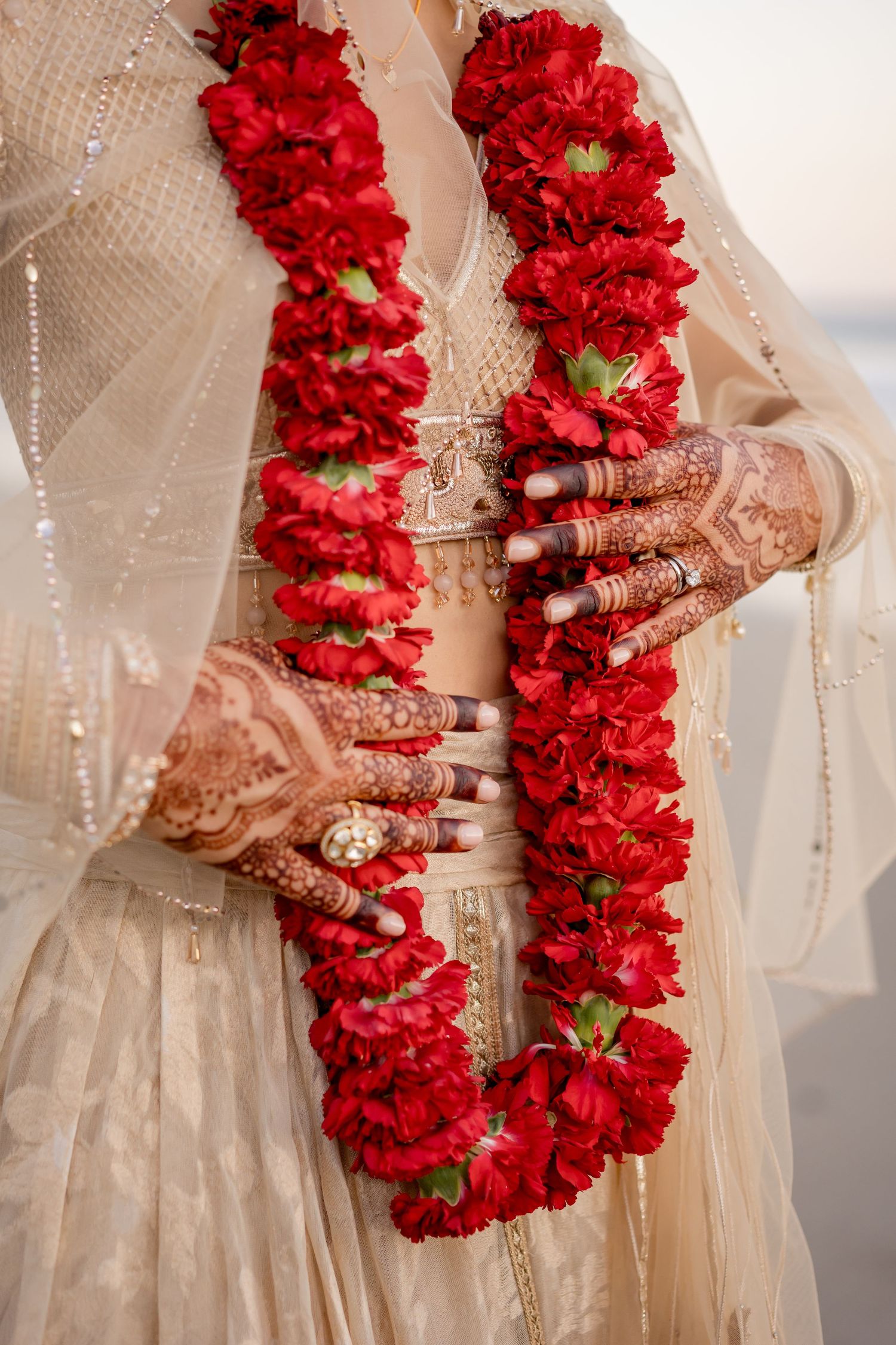 Vibrant red floral leis and intricate bridal henna celebrating hindu cultural wedding traditions during a luxury destination wedding.