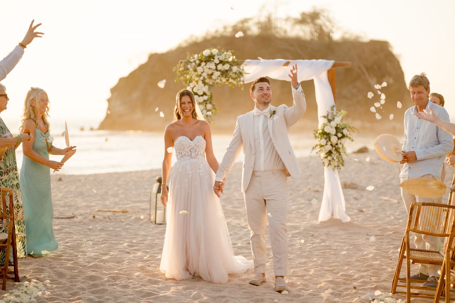 Newlyweds walking down the aisle after an oceanfront wedding ceremony as guests celebrate in Nosara Beach, Costa Rica.