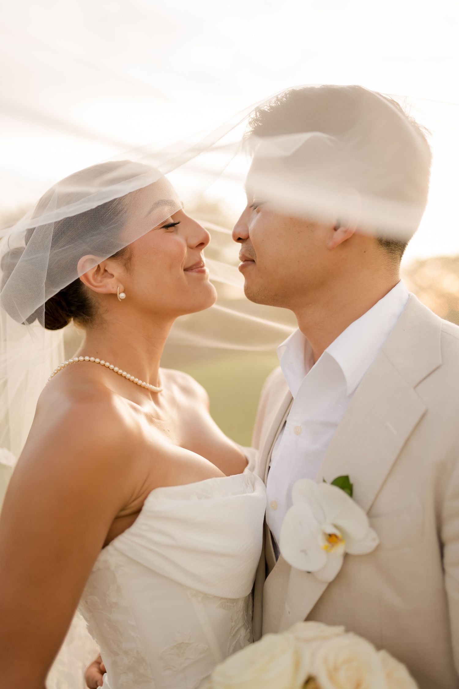 Editorial close-up wedding portrait featuring soft golden hour light, a flowing bridal veil, and an intimate moment between newlyweds Andaz